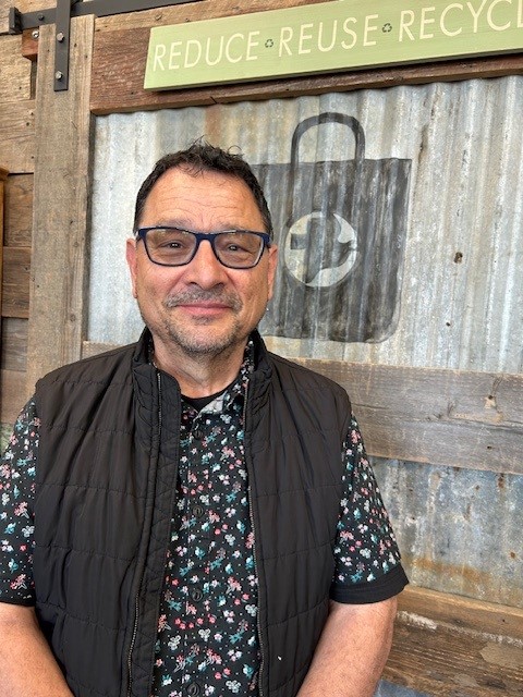 A picture of Carlos Ostia standing in front of the MCC Thrift logo.