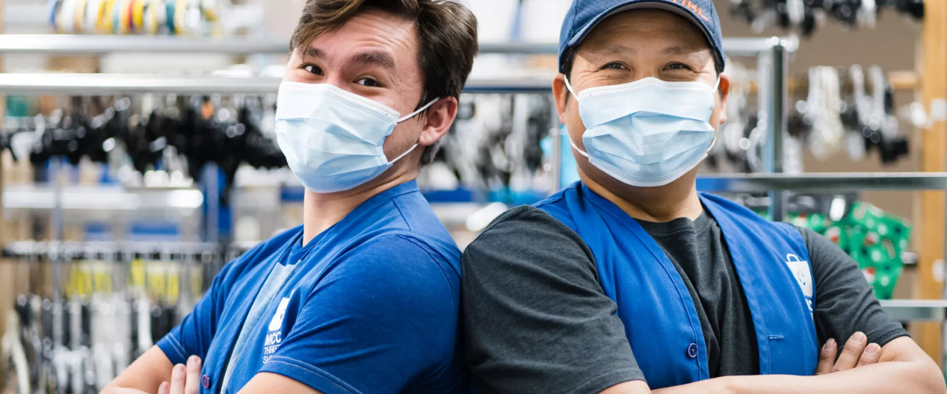 Two thrift employees back to back smiling behind surgical masks