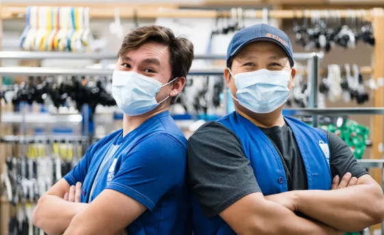 Two thrift employees back to back smiling behind surgical masks