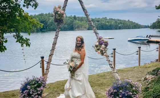 Grace Marcy Bayles, standing in front of a lake, wearing her wedding dress on her wedding day.