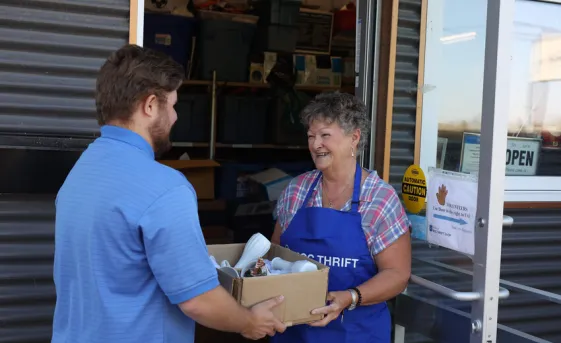 A man donating a box of pre-owned goods to an MCC Thrift shop volunteer.