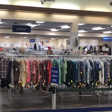 Two women shopping in the clothing aisles of a thrift shop.