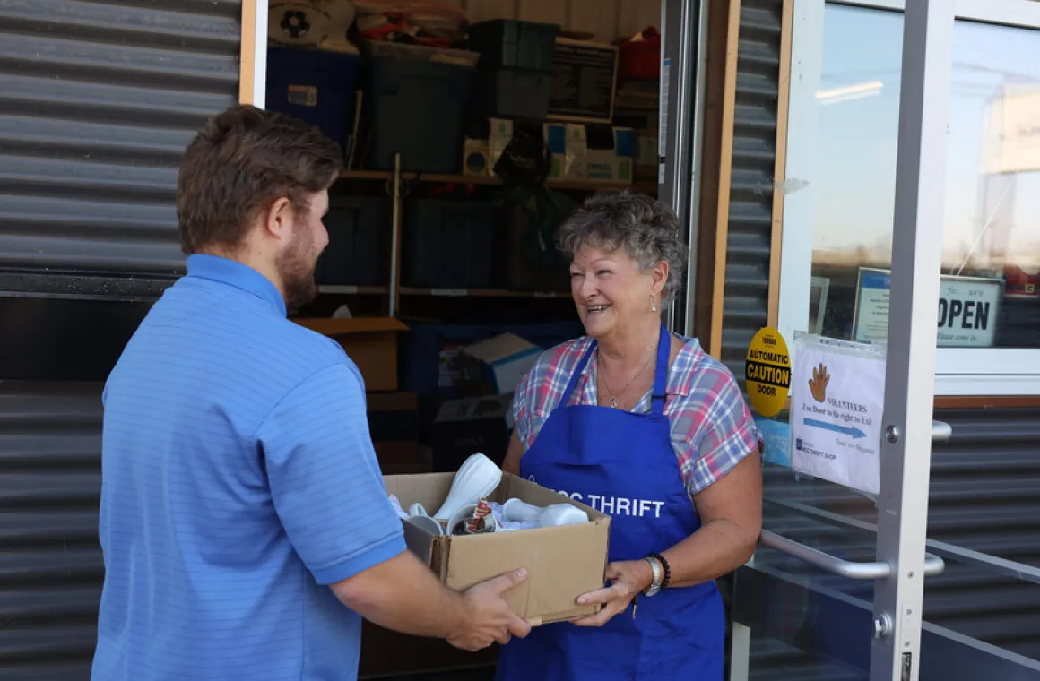 A man donating a box of pre-owned goods to an MCC Thrift shop volunteer.