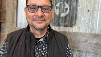 A picture of Carlos Ostia standing in front of the MCC Thrift logo.