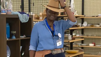 A smiling woman wearing a blue shirt and a beige hat.